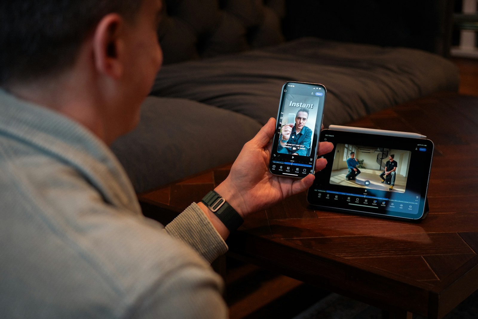 Person holding a phone and watching a vertical video while a tablet shows an edited scene.